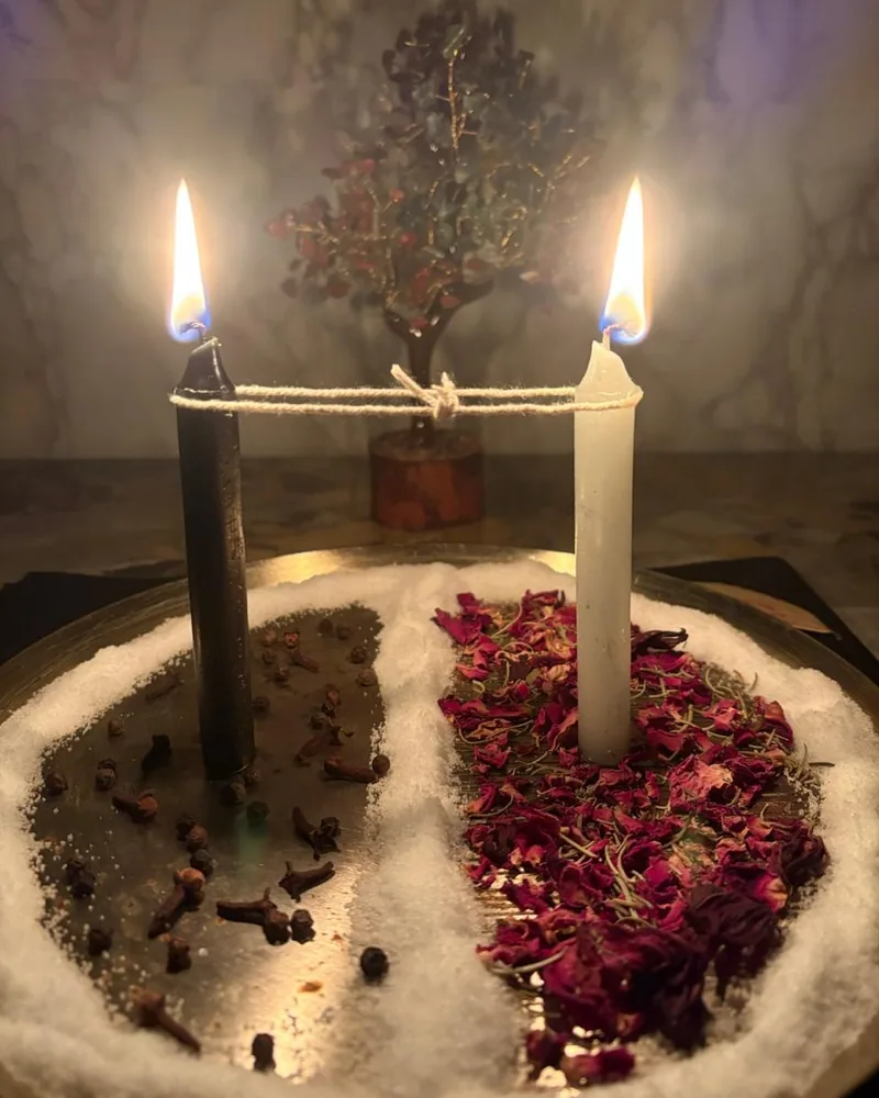 Black and white candles joined by a cord over salt and rose petals
